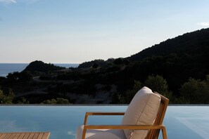 A wooden chair with a cushion by an infinity pool overlooking a coastal landscape. - Scirocco Telemachos 1 BED (Lefkada)