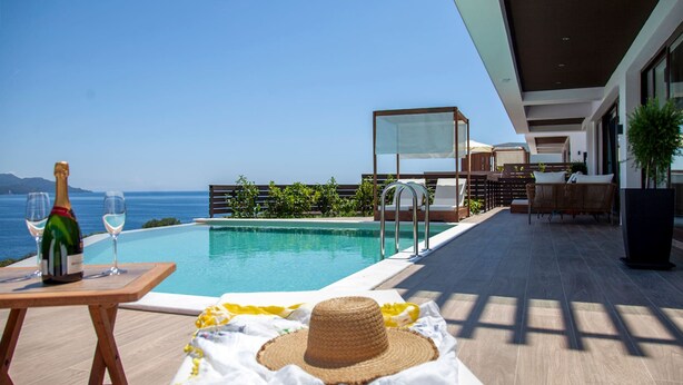 Un espace aménagé au bord de la piscine, avec vue sur la mer, une bouteille de champagne et un chapeau de paille posé sur une serviette.