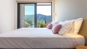 Ein Schlafzimmer mit einem großen Bett, einem Holznachttisch und Blick ins Freie.