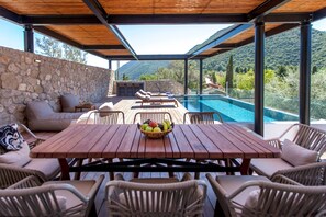 An outdoor dining area with a pool, stone wall, and mountain views. - Desimi Villa Naya in Desimi (Lefkada)