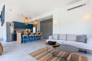 A modern living room with a sofa, a coffee table, and a kitchen area with a dining set. - Desimi Villa Naya in Desimi (Lefkada)