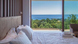 A bedroom with a large bed, a view of the sea, and a chair. - Zavia Villa ENA 2B Syvota (Igoumenitsa)