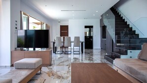 A modern living room with a flat-screen TV, a sofa, a coffee table, and a dining area with chairs. - Zavia Villa ENA 2B Syvota (Igoumenitsa)