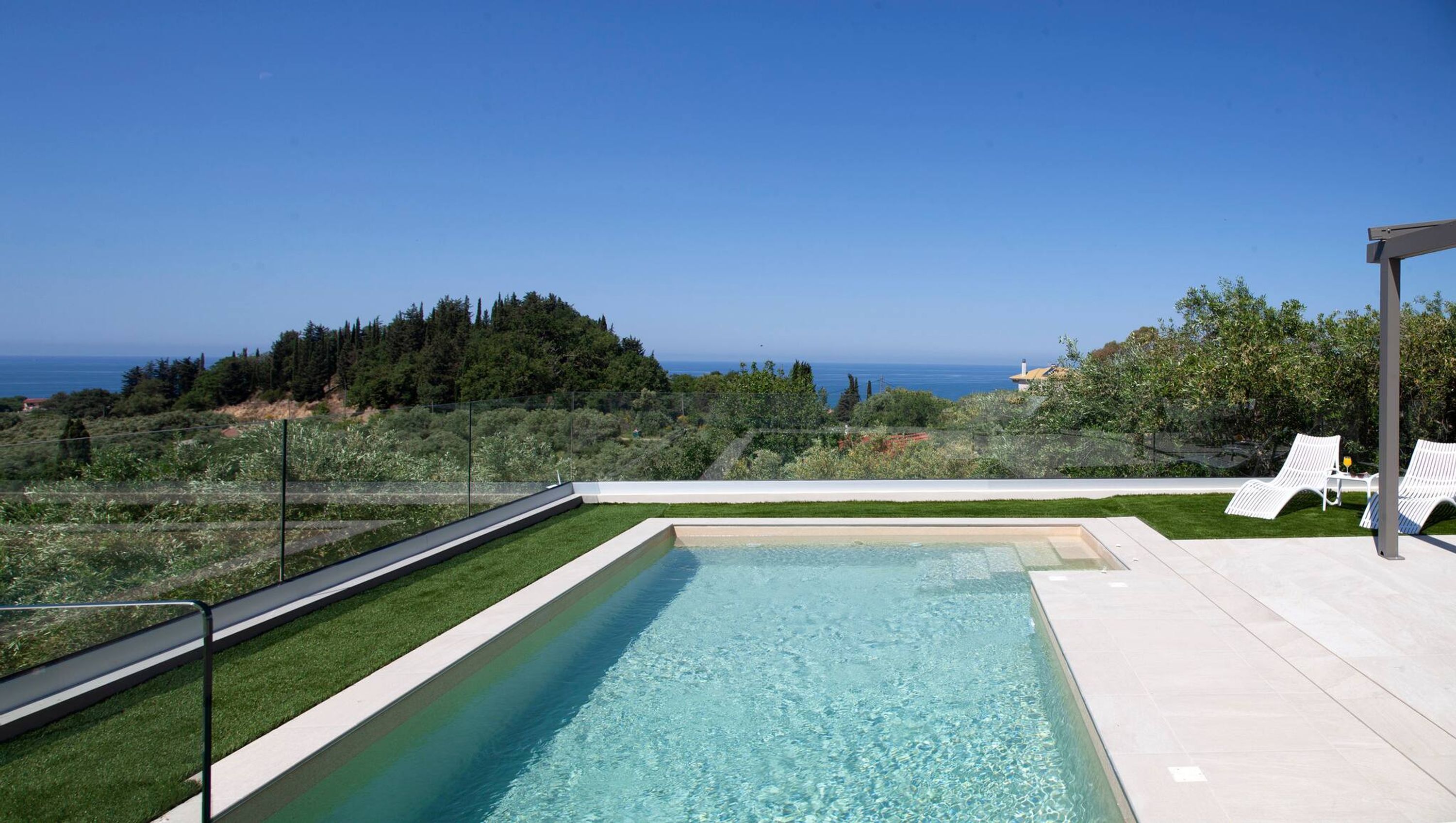 Une piscine rectangulaire à l’eau claire, entourée d’une terrasse blanche et d’une rambarde en métal.