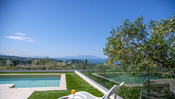 A poolside area with a view of the sea, a table with a drink, and lounge chairs. - Lumiere Villa Andromeda 3 (Preveza)