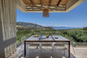 A terrace with a table and chairs, overlooking a scenic landscape with mountains and the sea. - Villa Eptanisa in Sivota (Lefkada)