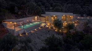 A modern villa with a swimming pool, outdoor seating, and a stone retaining wall.