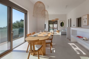 Un espace de salle à manger moderne, doté d’une grande table, de chaises et de luminaires suspendus.