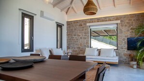 A modern interior with a stone wall, a wooden dining table, a sofa, and a TV mounted on the wall. - Smirties Villa Pasithea 4bed (Lefkada)