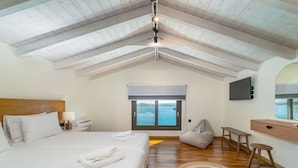 A bedroom with a large bed, a wooden ceiling, a view of the sea, a TV, and a desk. - Smirties Villa Pasithea 4bed (Lefkada)