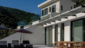 A modern building with a flat roof, large windows, and a terrace with seating. - Scirocco Odyssey 2 BED (Lefkada)