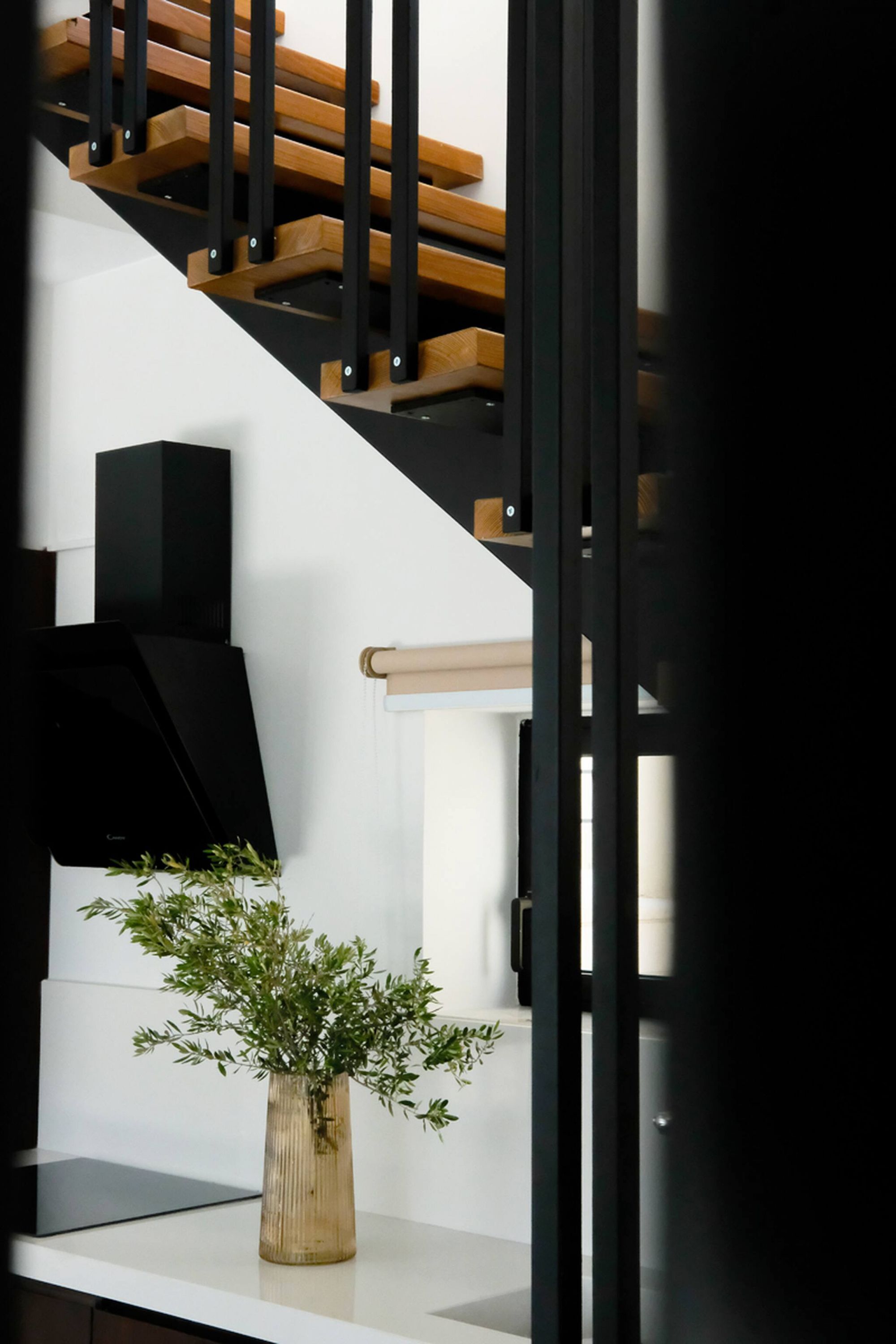 Eine moderne Treppe mit Holzboden und schwarzen Geländern, eine weiße Wand, ein schwarzer Lautsprecher und eine Vase mit Grünpflanzen auf einer weißen Oberfläche.