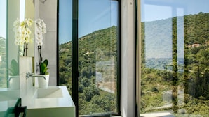 A modern bathroom with a large window, a white sink, and a potted plant. - Scirocco Odyssey 2 BED (Lefkada)
