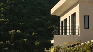 A modern building with a balcony, surrounded by dense forest. - Scirocco Odyssey 2 BED (Lefkada)