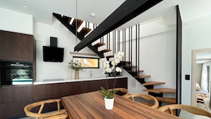 A modern kitchen with a built-in oven, a dining area with a wooden table and chairs, and a staircase with a black railing. - Scirocco Odyssey 2 BED (Lefkada)