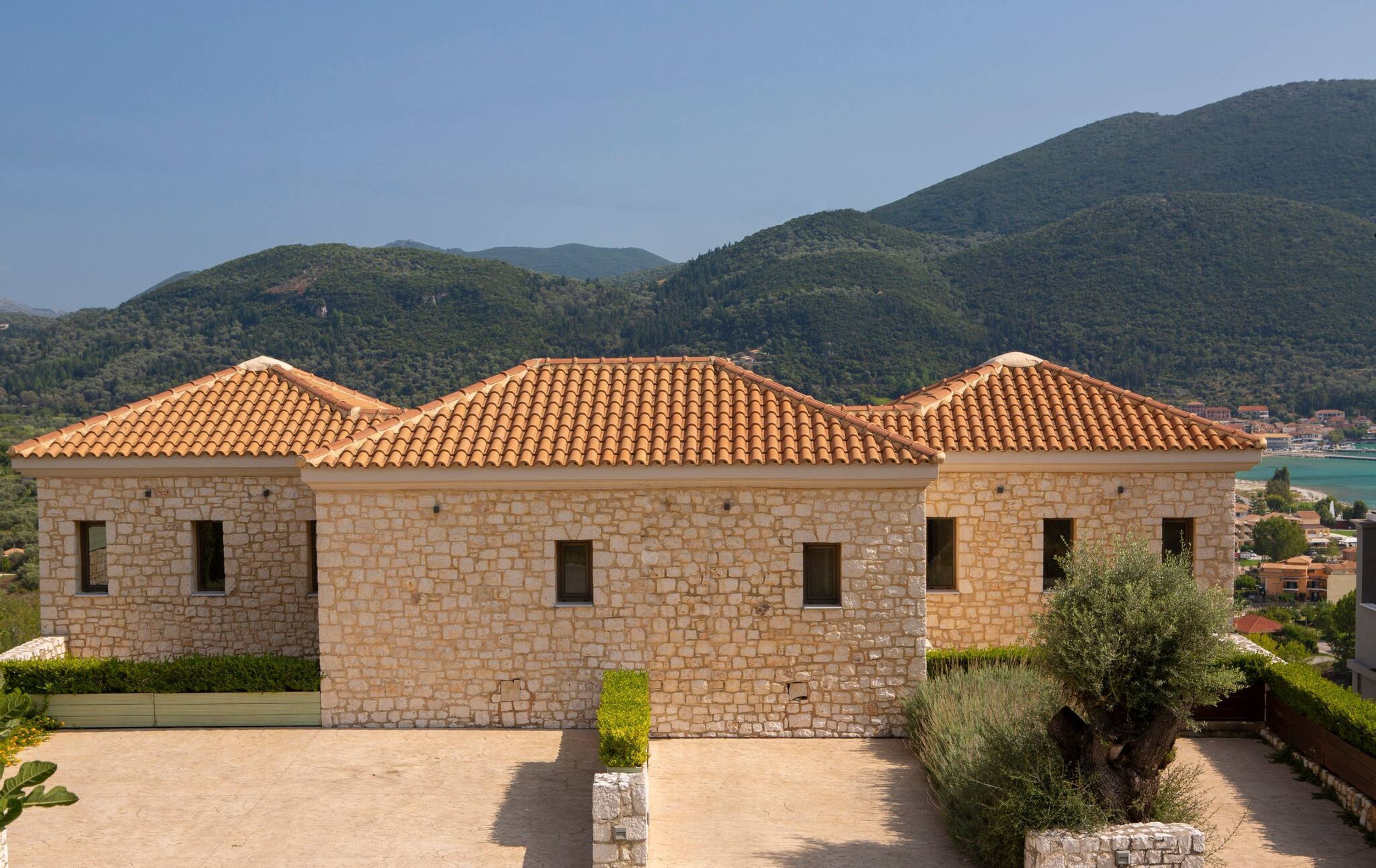 A stone building with a tiled roof, surrounded by greenery and mountains.