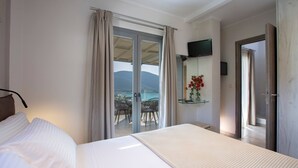 A hotel room with a bed, a TV, a sliding glass door to a balcony with a view, and a small table with a vase of flowers. - Aria 4 Ostria in Ponti (Lefkada)