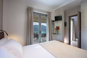 A hotel room with a bed, a TV, a sliding glass door to a balcony with a view, and a small table with a vase of flowers. - Aria 4 Ostria in Ponti (Lefkada)