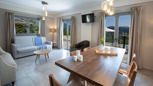 A modern living room with a sofa, dining table, chairs, and a TV mounted on the wall. - Aria 4 Ostria in Ponti (Lefkada)