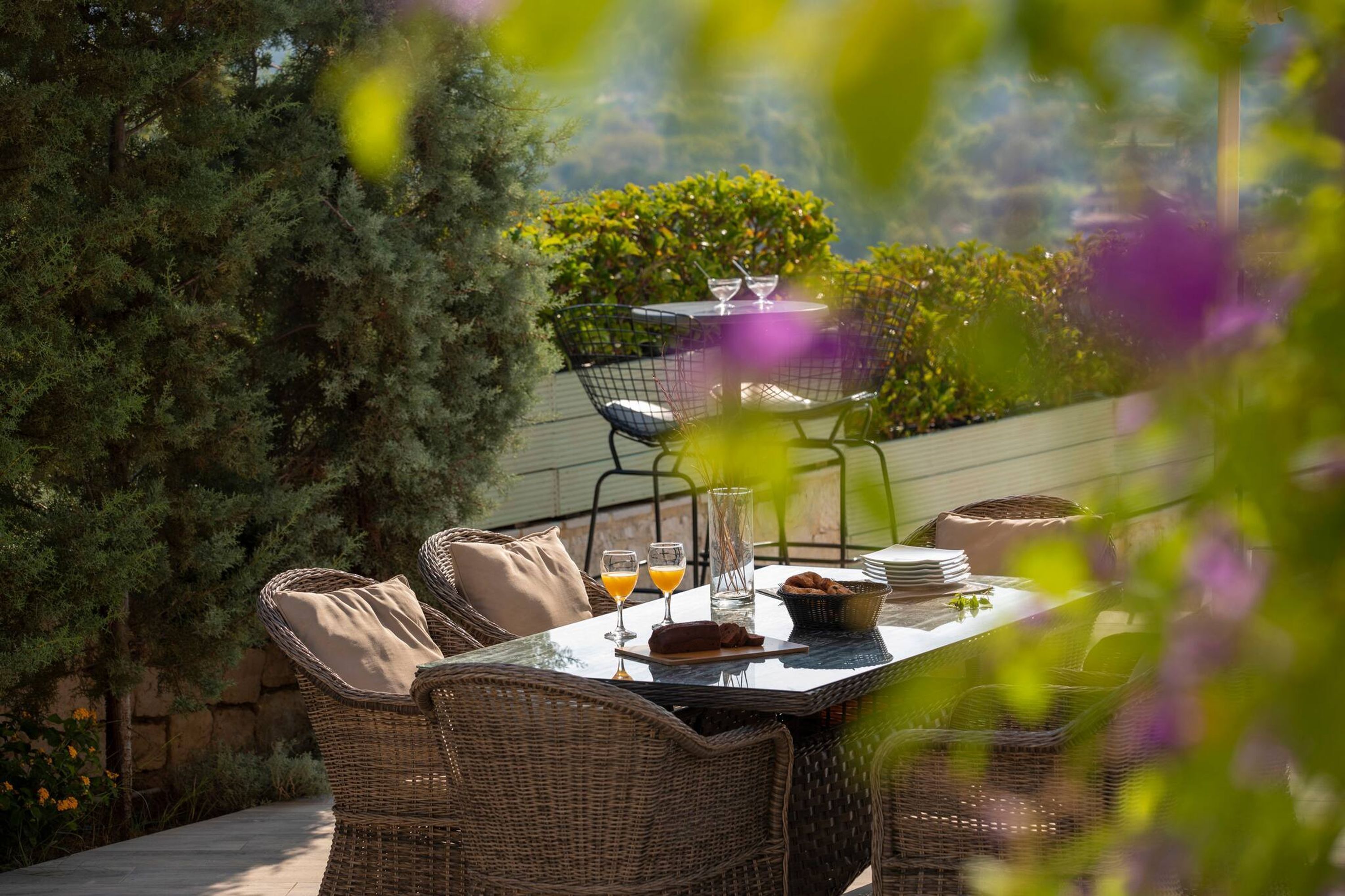 An outdoor dining area with wicker furniture, a table set with plates, glasses, and a basket.