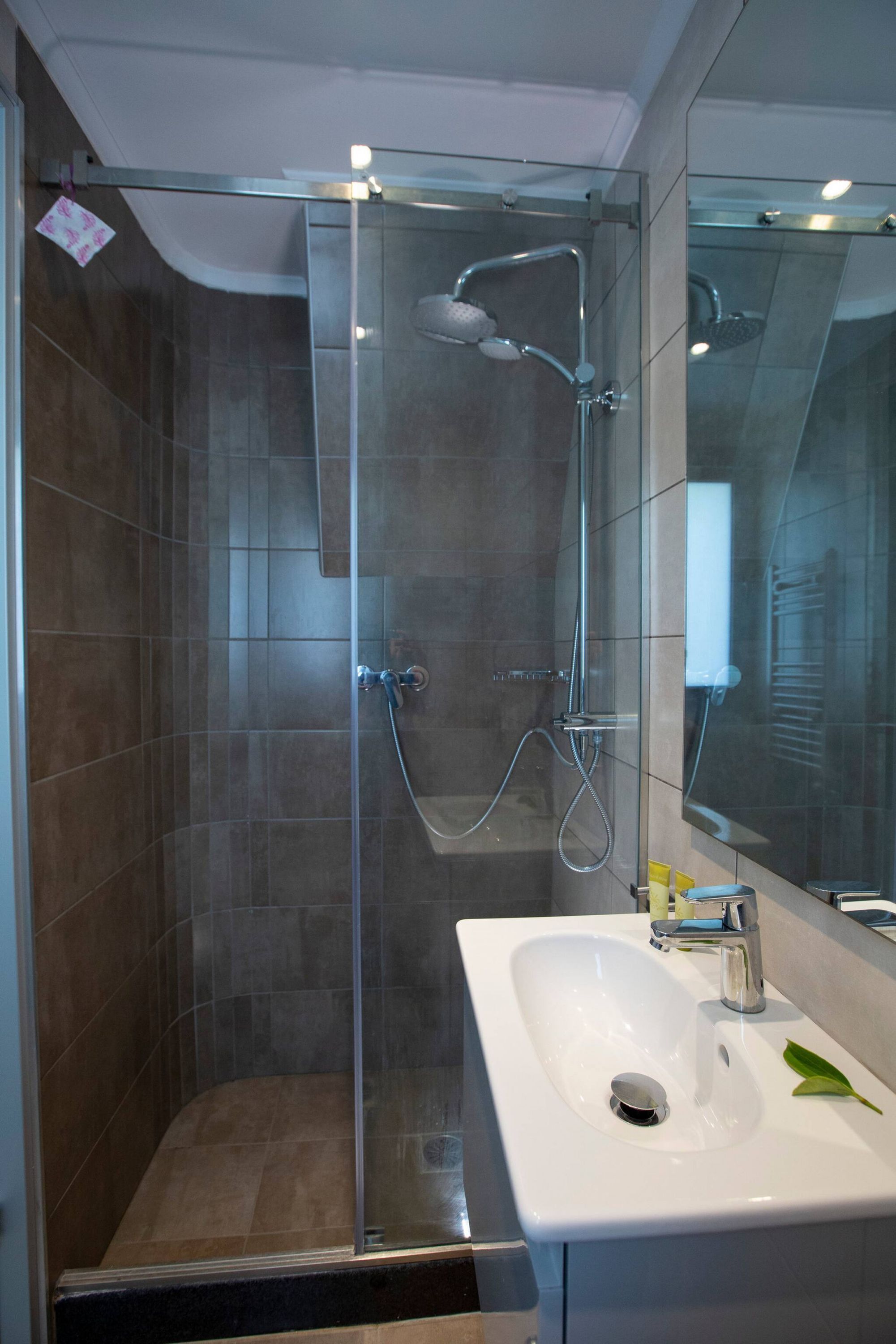 Un baño moderno con ducha envuelta en vidrio, un lavamanos blanco y un espejo grande.