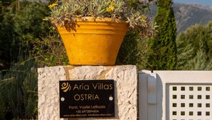 A stone wall with a sign for 'Aria Villas OSTRIA' and a yellow planter with plants. - Aria 4 Ostria in Ponti (Lefkada)