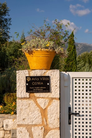 A stone wall with a sign for 'Aria Villas OSTRIA' and a yellow planter with plants. - Aria 4 Ostria in Ponti (Lefkada)