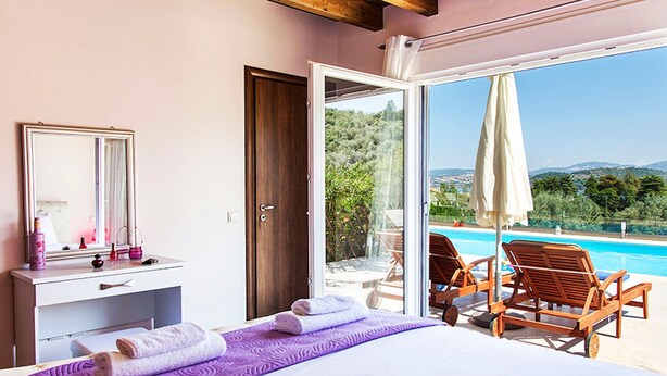Un dormitorio con una cama grande, un tocador con espejo y vistas a una piscina y montañas.