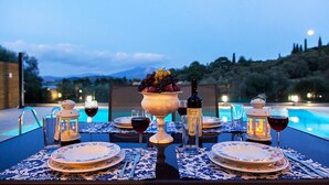 Mesa de comedor al aire libre con vista a la piscina, un cuenco de fruta, copas de vino y una botella de vino.
