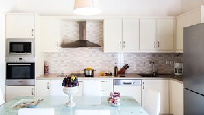 Una cocina con gabinetes blancos, una campana extractora de acero inoxidable, un microondas, un fregadero y un refrigerador.
