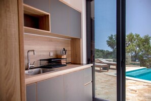 A modern kitchen with a built-in sink, wooden cabinets, and a view of a swimming pool. - Villa Dara AND Todd in Sivota (Lefkada)