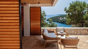 A balcony with wicker furniture, a stone floor, and a view of a coastal landscape.