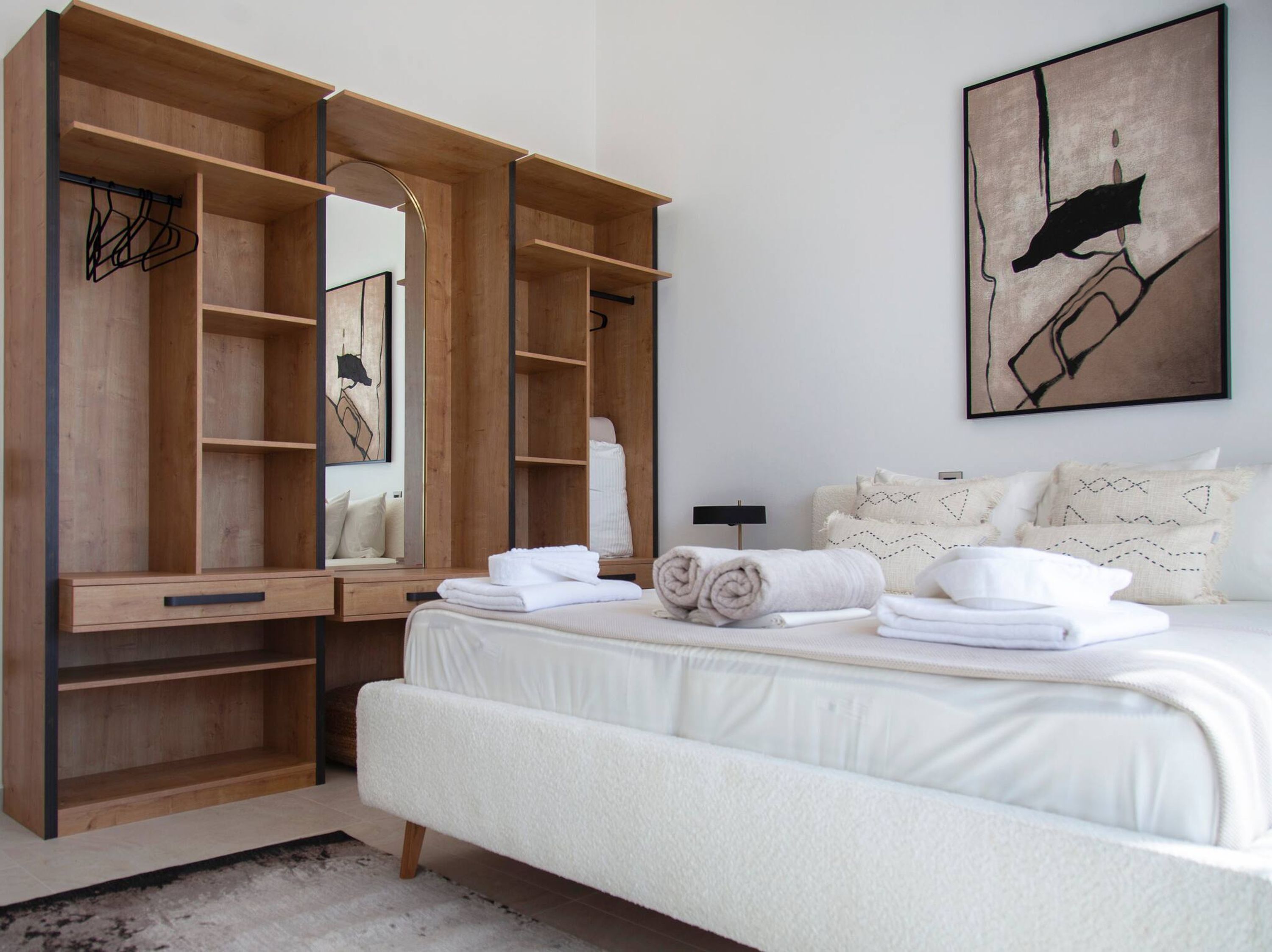 A bedroom with a large wooden wardrobe, a bed with white linens, and a painting on the wall.