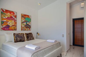 A hotel room with a bed, two leopard print pillows, a wall with colorful fish paintings, a door, and a lamp.