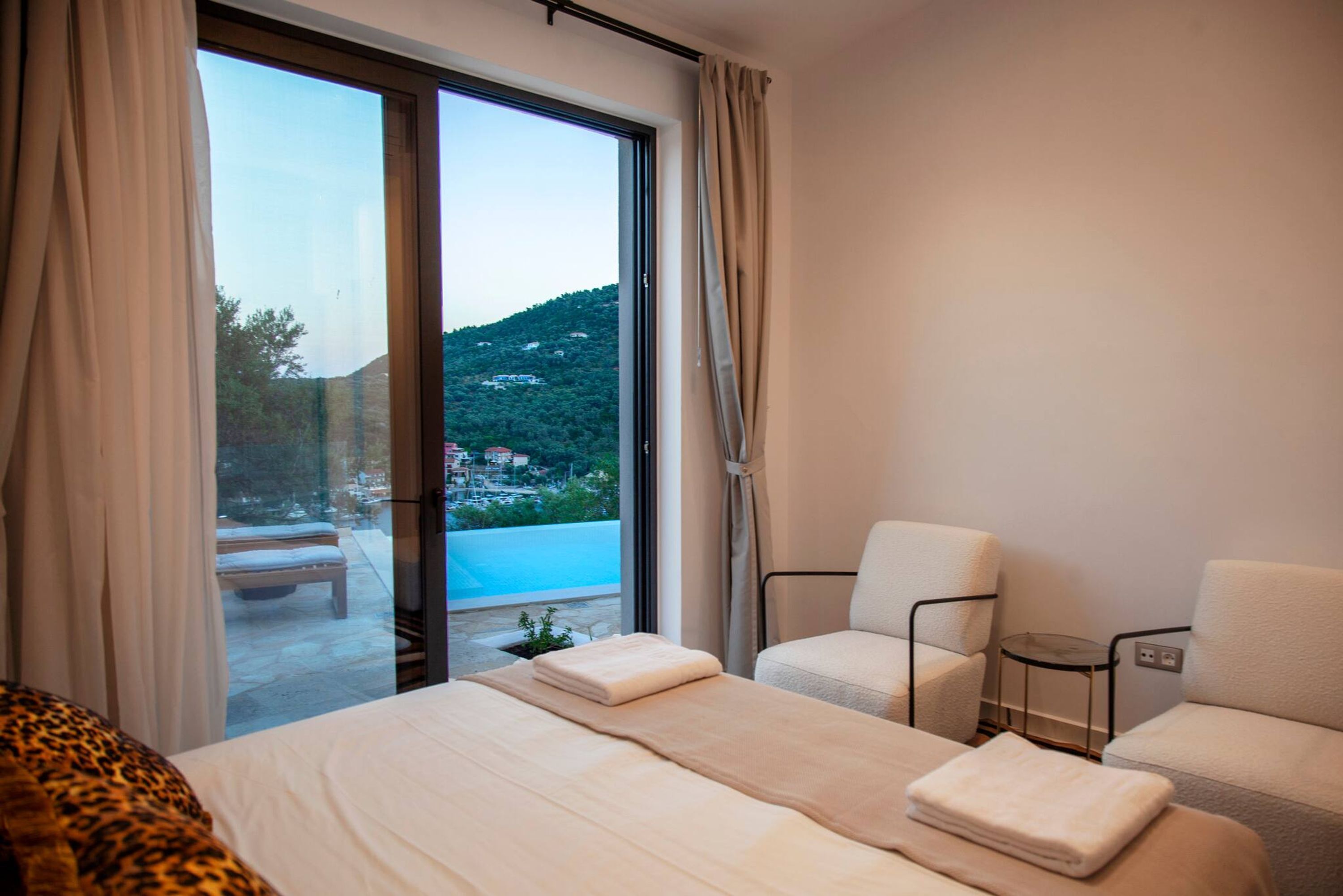 Une chambre d’hôtel avec un lit, deux chaises, une petite table et une vue sur une piscine et une colline.