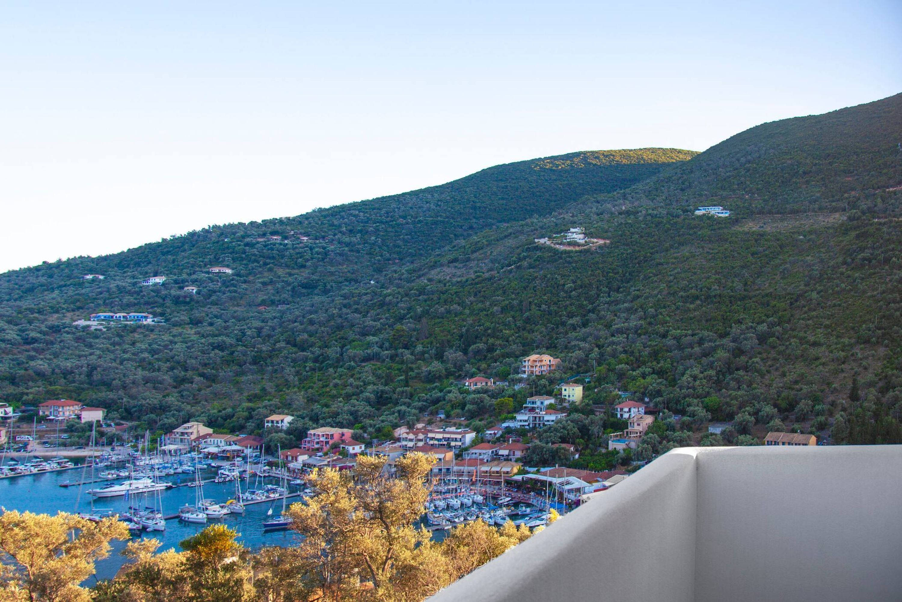 A coastal town with a marina, houses on hills, and a clear sky.