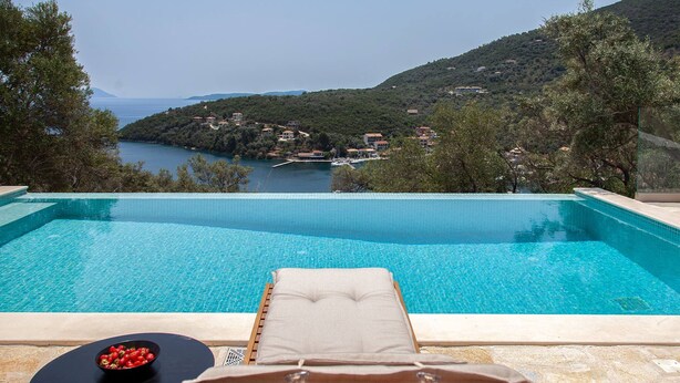 A pool with a lounge chair and table, overlooking a lake and hills.