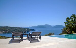 A poolside area with two chairs and a table, overlooking a scenic view of the sea and hills. - Villa Blauw in Vasiliki (Lefkada)