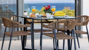 A dining table with wicker chairs, a glass top, and a view of the sea through large windows. - Z4 Delta 2bed in Lefkada (Lefkada)