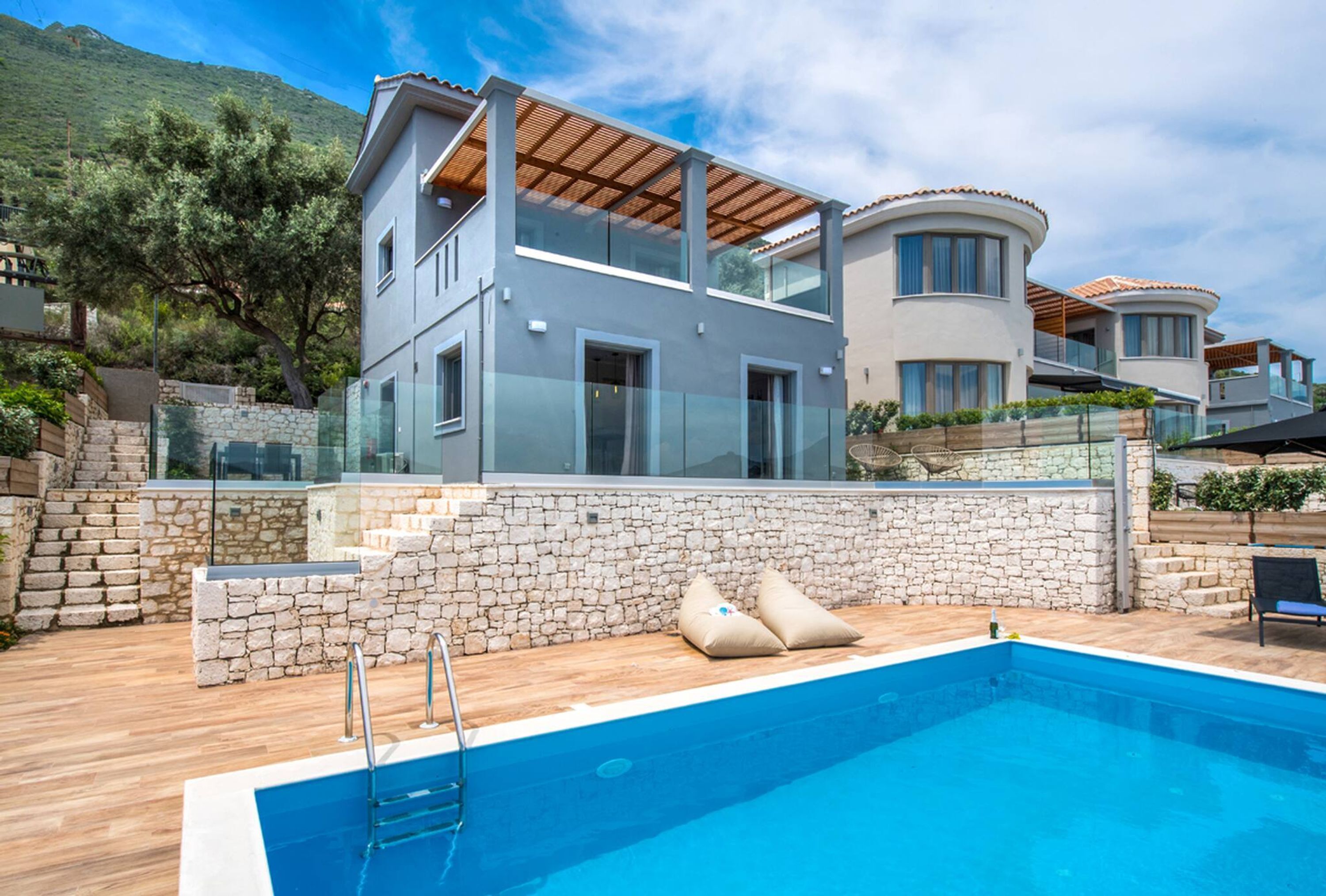 Una casa moderna de dos pisos con piscina, muros de piedra y terraza de madera.