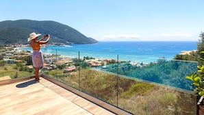 Eine Person auf einem Balkon mit Blick auf die Küste unter blauem Himmel.