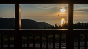 A sunset view through a window with a wooden railing, a distant mountain, and a fence in the foreground. - Vissala5 Alkanna in Vasiliki (Lefkada)