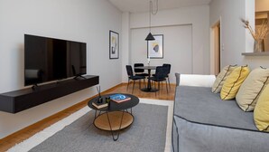 A modern living room with a flat-screen TV, a round coffee table, a sofa, and a dining area with chairs. - Beehive 2A in Athens (Athens)
