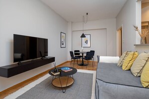 Ein modernes Wohnzimmer mit Flachbildfernseher, rundem Couchtisch, einer Couch und einem Essbereich mit Stühlen.