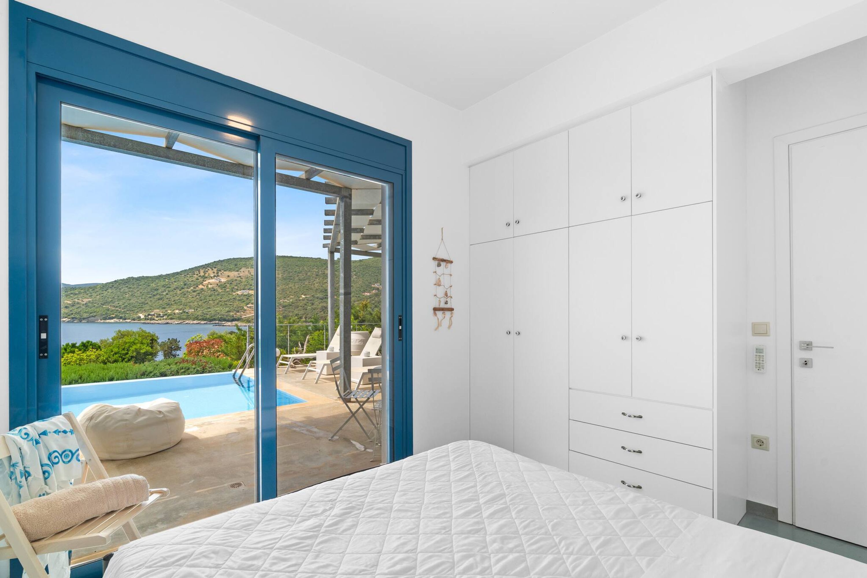 Ein Schlafzimmer mit Bett, Kleiderschrank und Blick auf Pool und Außenbereich mit Sitzgelegenheit.