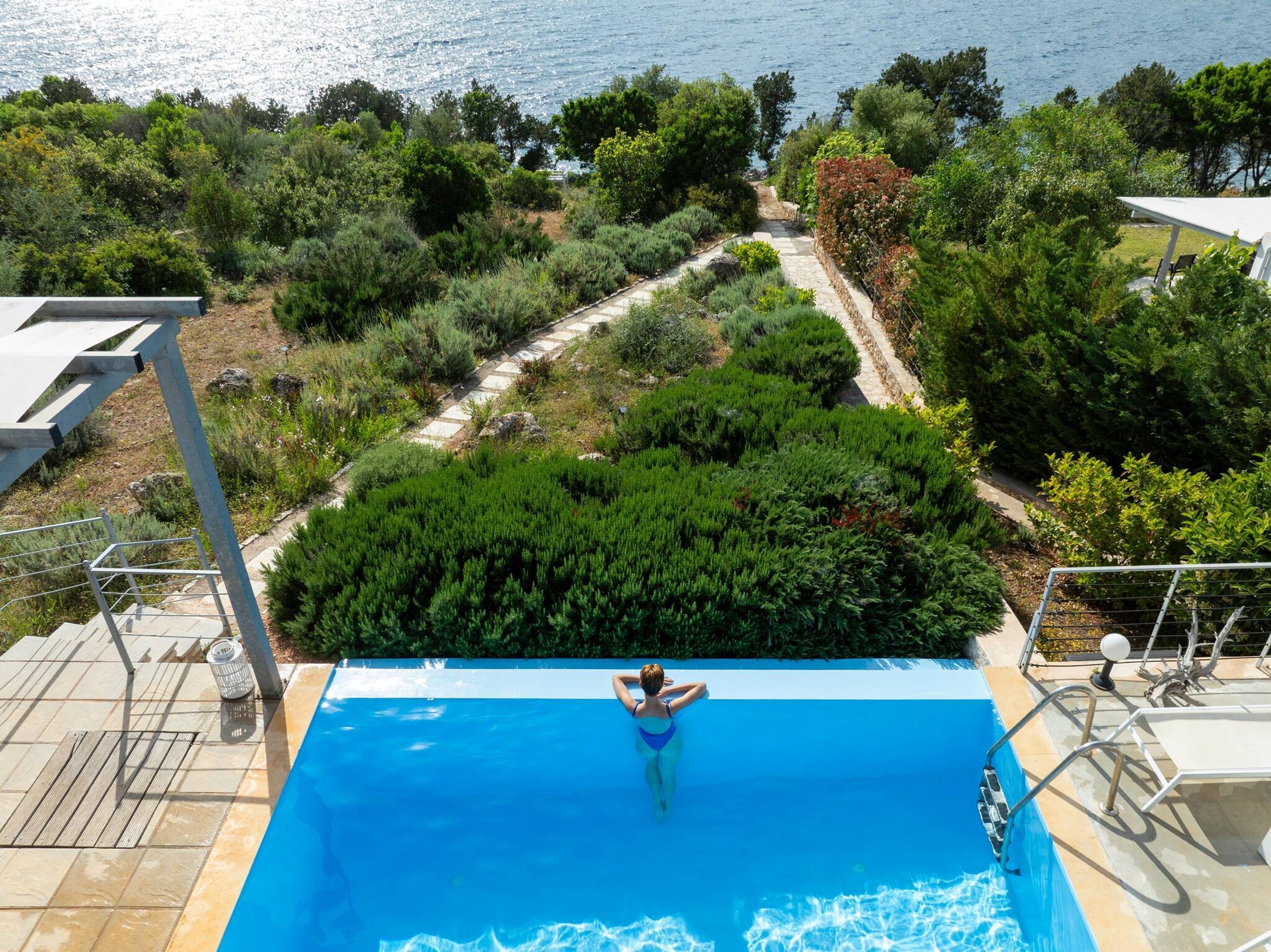 A swimming pool with a person in the water, surrounded by greenery and overlooking a body of water.