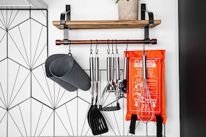 Een keuken met een hangende rek met verschillende keukengerei, een zwarte spatel en een oranje tas met tekst.