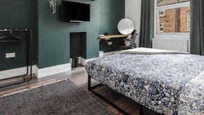 A bedroom with a bed, a television mounted on the wall, a small table, and a window with a view of a brick building. - 3 Floors Loft 2mins to Train Patio Parking (Liverpool)