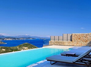 A pool with clear blue water, lounge chairs, and a stone wall overlooking a coastal landscape. - FR Villa Symposium in Sivota (Lefkada)