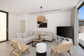 A modern living room with a sofa, two wicker chairs, a coffee table, a TV, and a hanging light fixture. - FR Villa Symposium in Sivota (Lefkada)